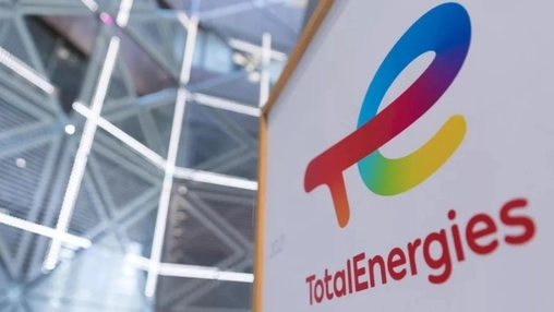 Close-up of TotalEnergies logo on white panel with blurred glass and steel architecture in the background